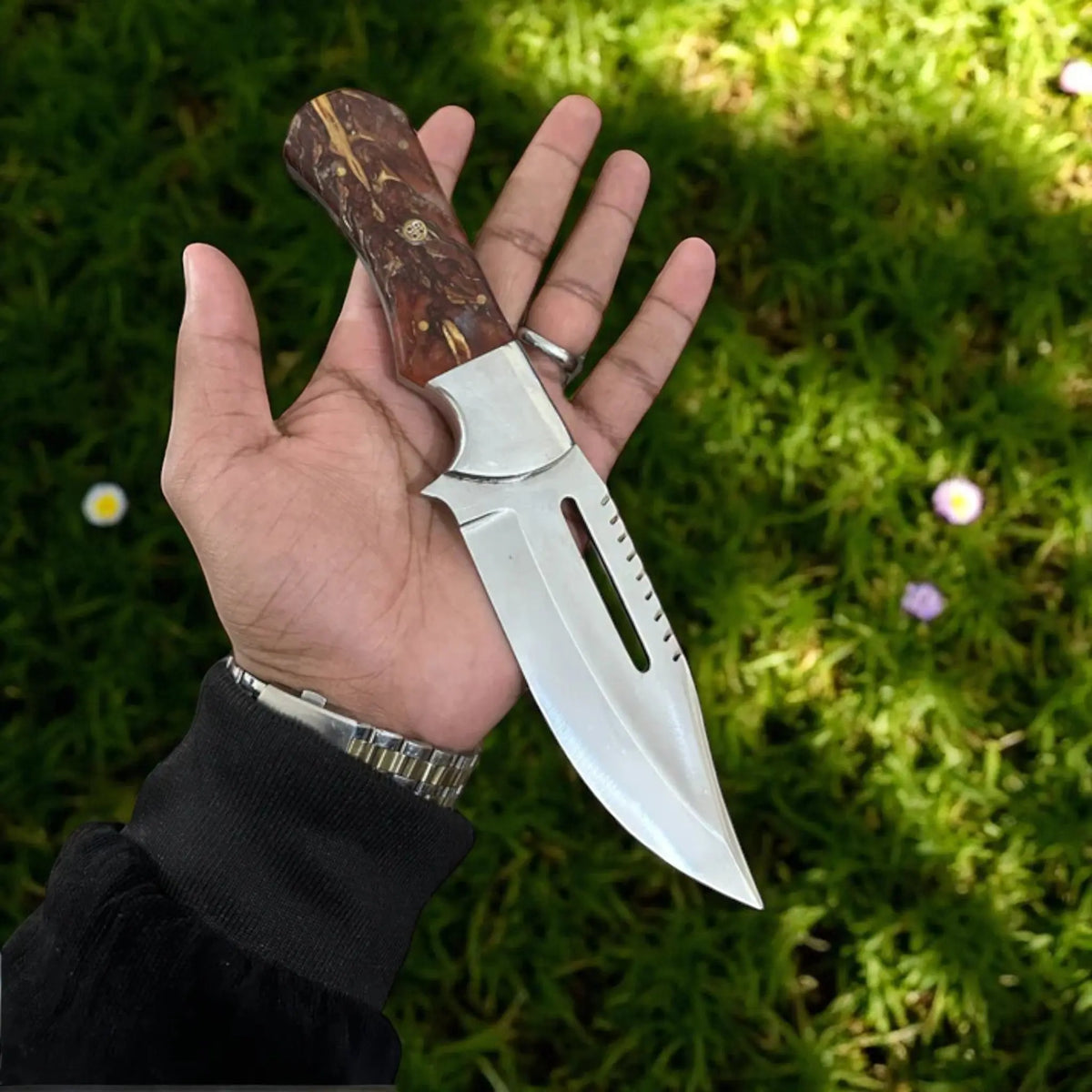 The Emberfang hunting knife by Arham Cutlery featuring a brown pine cone resin handle and a polished D2 steel blade, displayed in hand over grass.