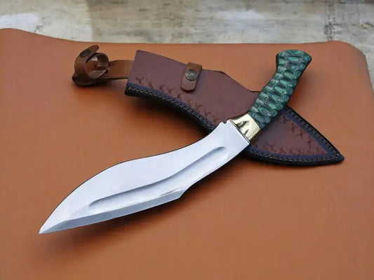 A curved fixed-blade knife with a silver blade, gold-toned bolster, and textured green handle, displayed with a brown leather sheath on a brown leather surface.