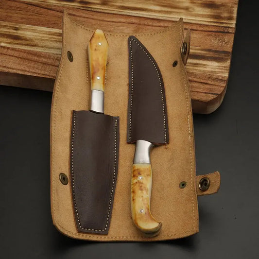 A fixed-blade knife with a polished bone handle and a dark brown leather sheath, displayed alongside a matching tan leather knife case on a dark surface with a wooden board in the background.