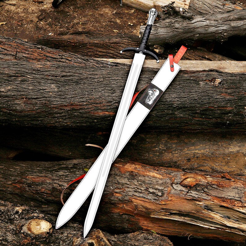 A silver-colored sword with a black wrapped handle and a matching white sheath with red accents, displayed diagonally on a rustic background of weathered logs.