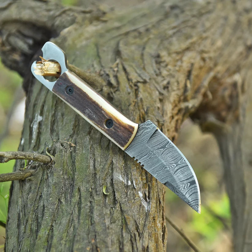 A custom fixed-blade knife with a Damascus steel blade and a dual-toned wooden handle, shown resting on a textured tree trunk in an outdoor setting.