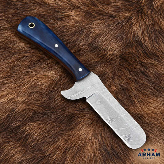 A fixed-blade knife with a patterned Damascus steel blade and a dark blue wooden handle, displayed diagonally on a brown fur background. The ARHAM Cutlery logo is visible in the bottom right corner.