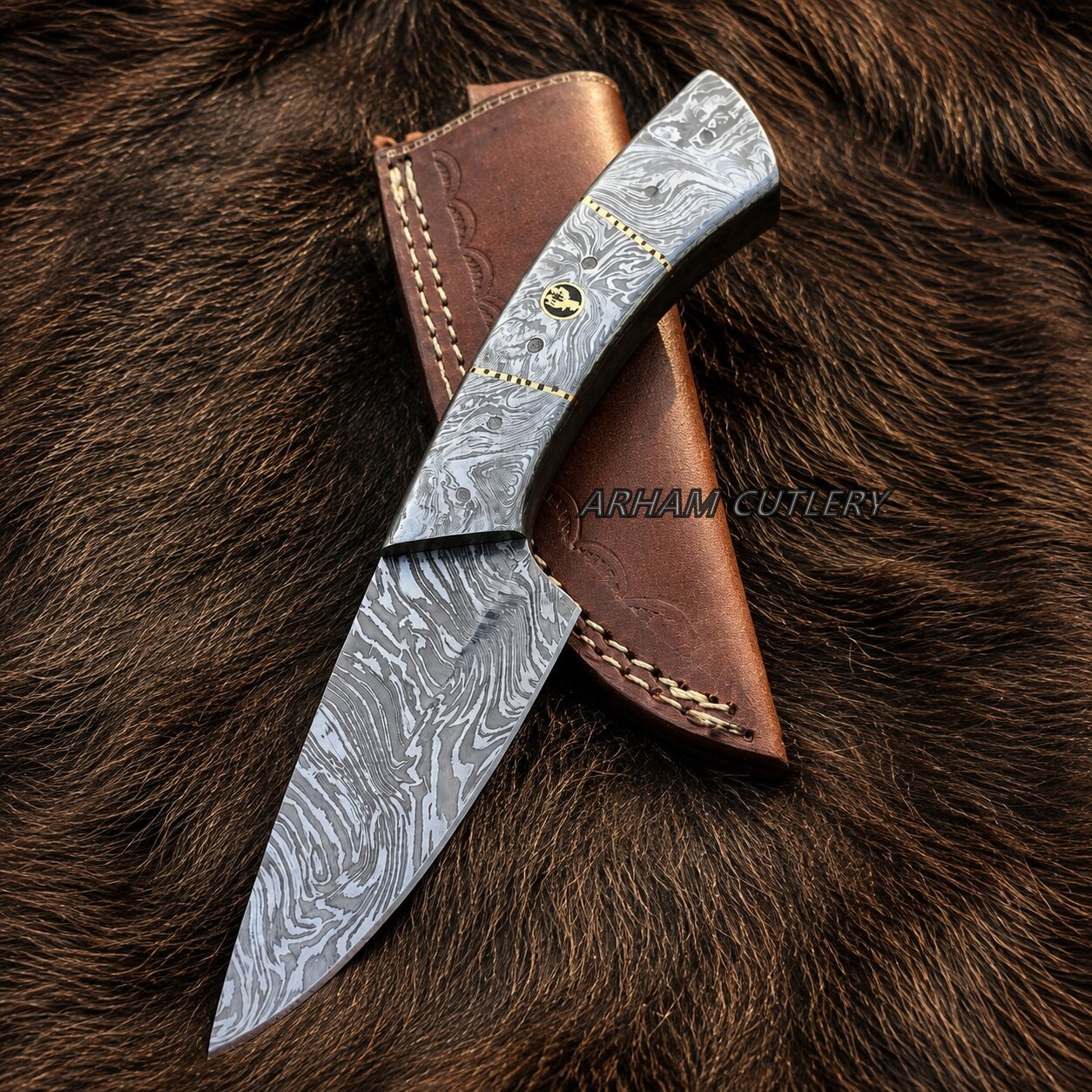 A Damascus steel fixed-blade knife with a wavy gray pattern blade, a brown leather sheath, and brass hardware, displayed diagonally on a brown fur background. A watermark for 'ARHAM CUTLERY' is visible across the center.