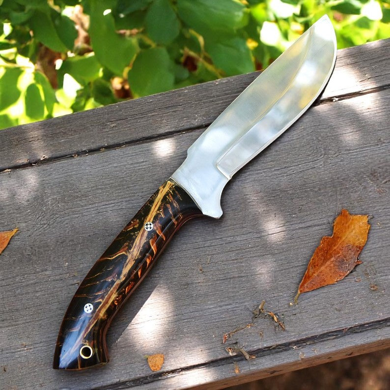 Handmade D2 steel hunting knife with black and amber resin handle on wooden surface – Arham Cutlery