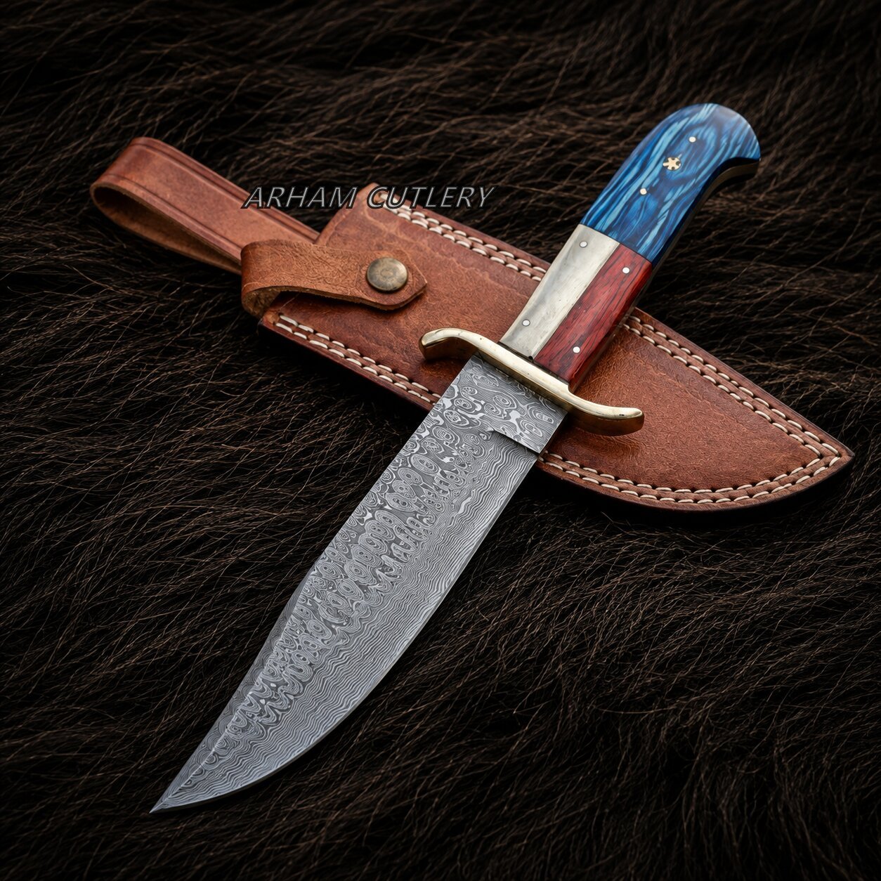A custom Damascus steel fixed-blade knife with a blue and red handle, displayed diagonally on its brown leather sheath over a dark brown fur background. A watermark for 'ARHAM GUTLERY' is visible across the center.