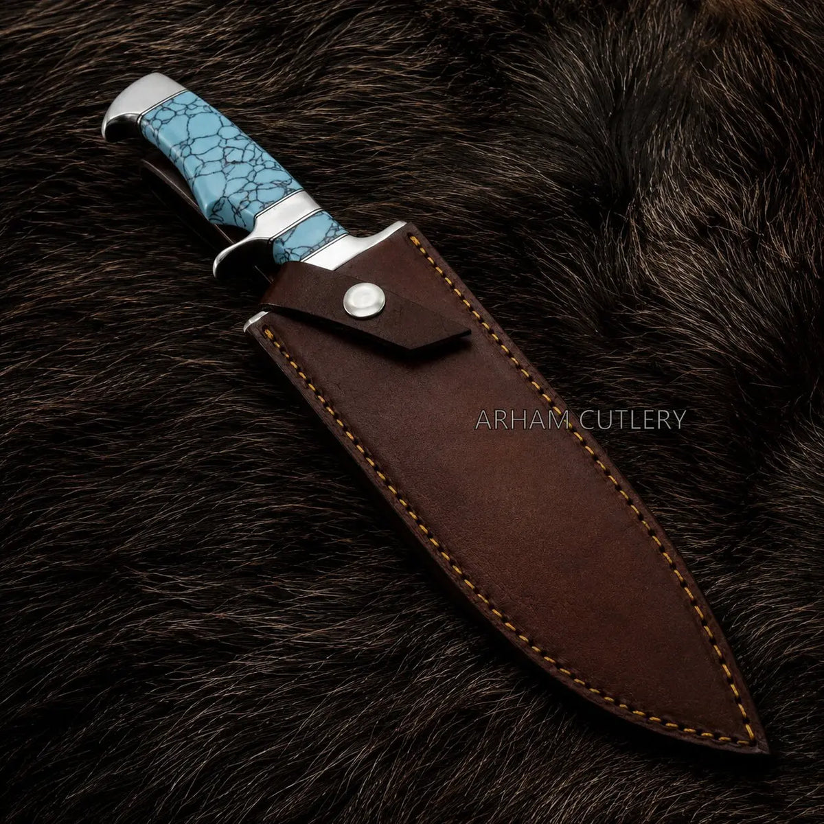 A fixed-blade knife with a textured turquoise blue handle and silver bolster, shown partially sheathed in a dark brown leather sheath with tan stitching, placed on a dark brown fur background. The brand name 'ARHAM CUTLERY' is watermarked on the sheath.
