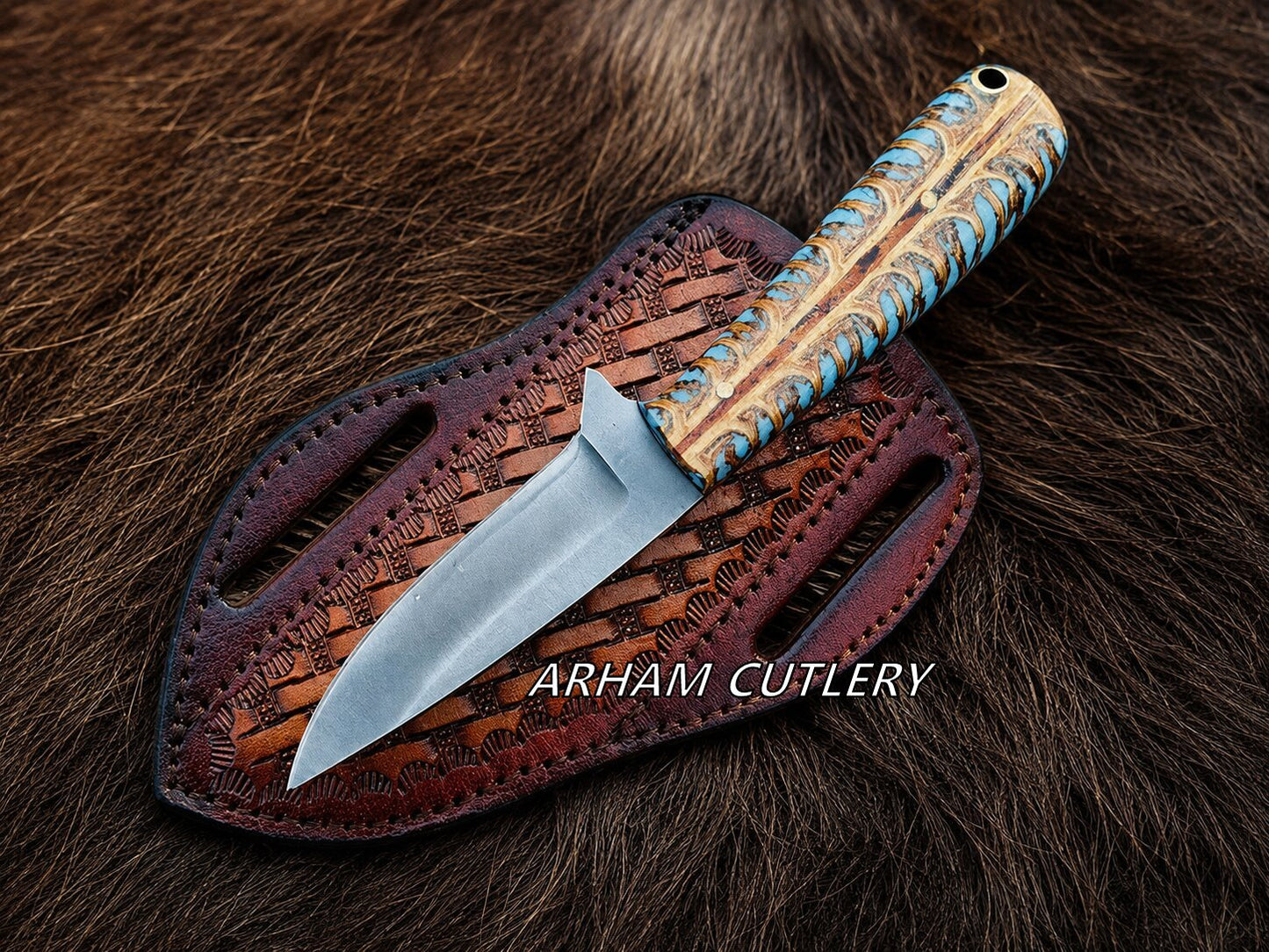 A fixed-blade knife with a textured tan and blue wrapped handle and a silver steel blade, resting on a brown leather sheath over a dark brown fur background. The text 'ARHAM CUTLERY' is overlaid on the image.