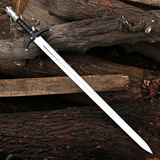 A long silver-colored sword with a black wrapped handle and silver pommel, resting diagonally on a rustic background of dark wooden logs.