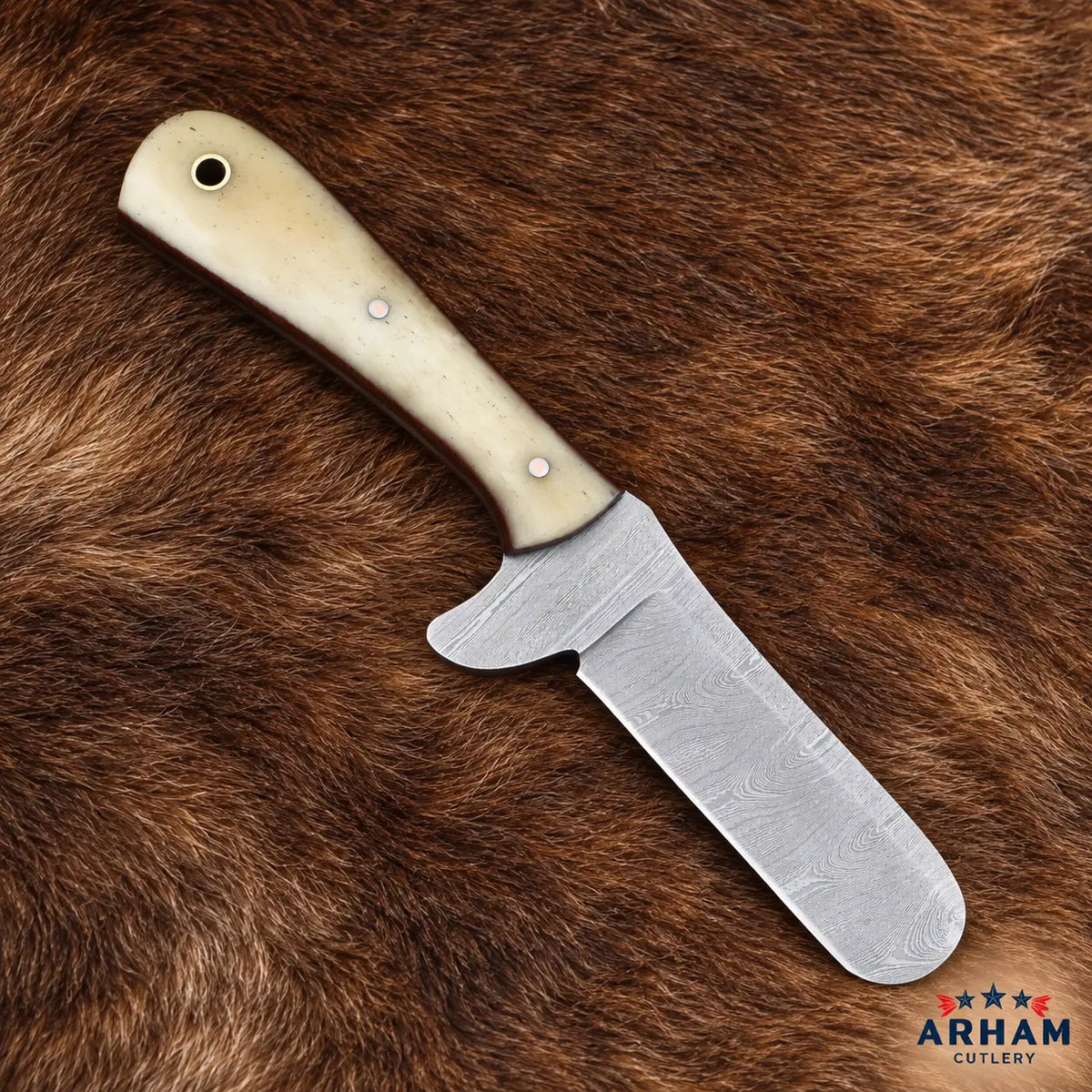 A fixed-blade knife with a patterned Damascus steel blade and a cream-colored bone handle, displayed diagonally on a brown fur background. The Arham Cutlery logo is visible in the bottom right corner.
