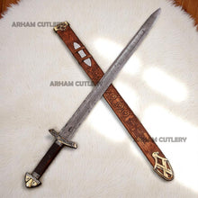 Cargar imagen en el visor de la galería, Hand-forged Viking Damascus steel sword with engraved wooden scabbard and ornate brass fittings displayed on a dark wooden background
