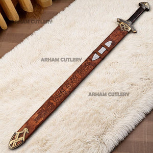 Hand-forged Viking Damascus steel sword with engraved wooden scabbard and ornate brass fittings displayed on a dark wooden background