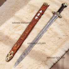 Cargar imagen en el visor de la galería, Hand-forged Viking Damascus steel sword with engraved wooden scabbard and ornate brass fittings displayed on a dark wooden background
