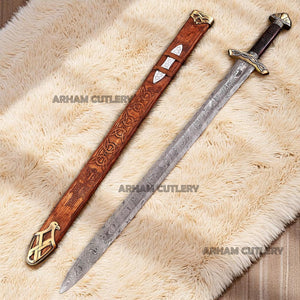 Hand-forged Viking Damascus steel sword with engraved wooden scabbard and ornate brass fittings displayed on a dark wooden background