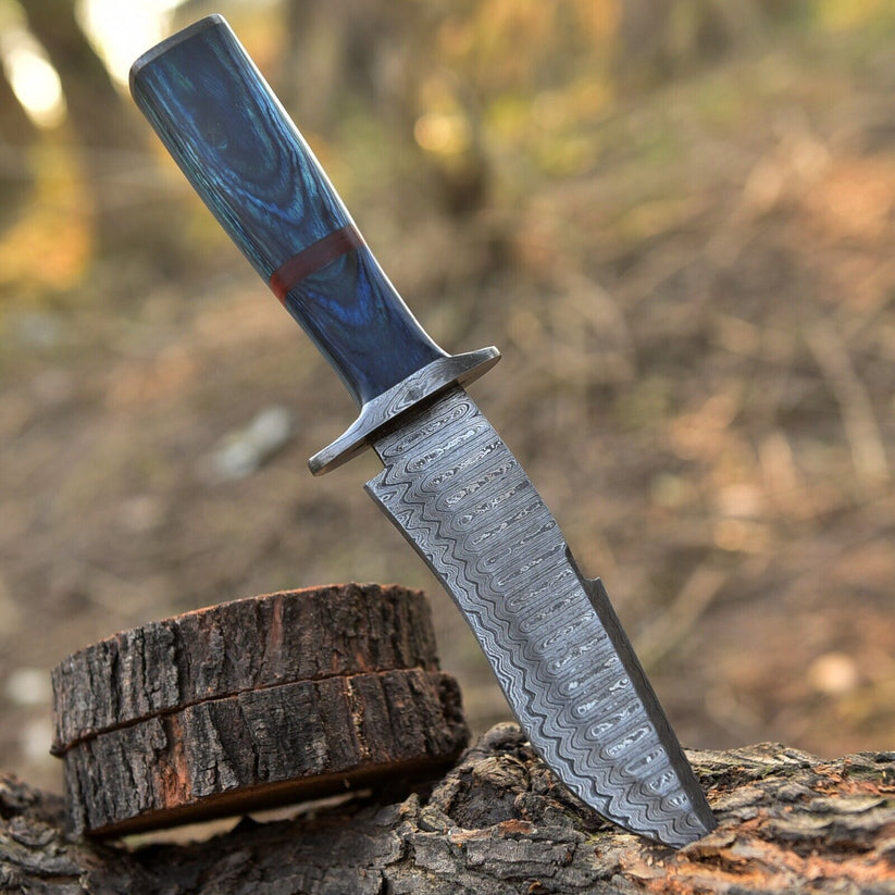 A fixed-blade knife with a patterned steel blade and a blue marbled handle, resting on a log outdoors with a blurred forest background.