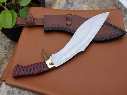 A fixed-blade knife with a silver blade, gold bolster, and textured reddish-brown handle, displayed next to its brown leather sheath on a brown leather surface.