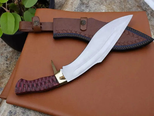 A fixed-blade knife with a silver blade, gold bolster, and textured reddish-brown handle, displayed next to its brown leather sheath on a brown leather surface.