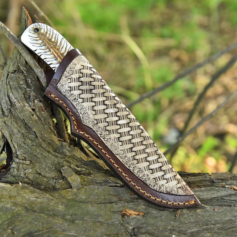 A fixed-blade knife with a textured woven-pattern handle and a dark brown leather sheath, resting on a weathered log in an outdoor forest setting.