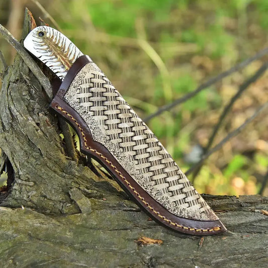 A fixed-blade knife with a textured woven-pattern handle and a dark brown leather sheath, resting on a weathered log in an outdoor forest setting.