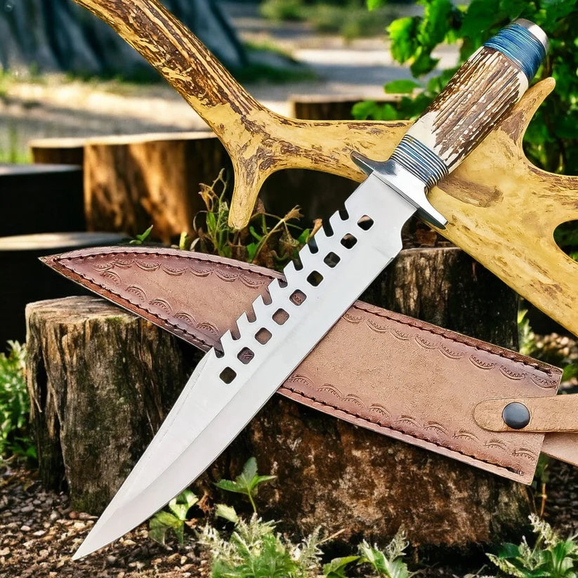 A fixed-blade knife with a silver blade featuring a square-hole cutout pattern near the base, resting on a brown leather sheath. The sheath and a yellow antler-like wooden prop are placed on rustic tree stumps in an outdoor forest setting.