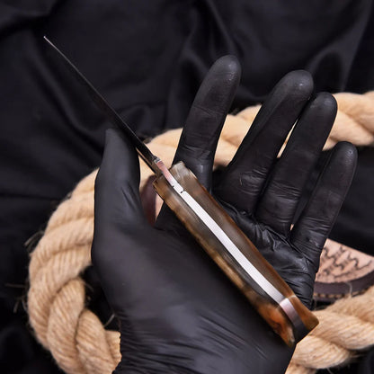 A close-up of a hand wearing a black glove holding a folding knife with a polished brown handle and a silver blade, set against a dark background with a coiled tan rope.