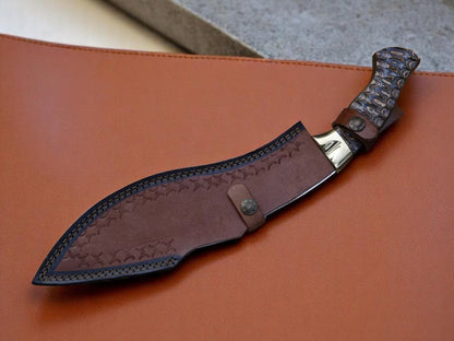 A fixed-blade knife with a textured handle and a brown leather sheath, displayed diagonally on a brown leather surface.
