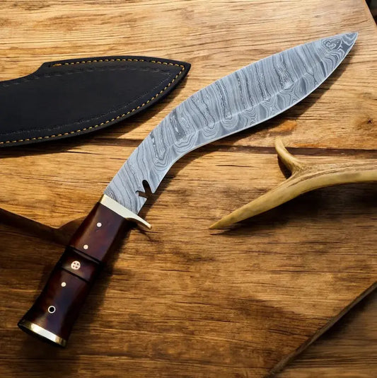 A curved Damascus steel fixed-blade knife with a dark brown wooden handle and brass pins, displayed next to its black leather sheath on a rustic wooden surface.