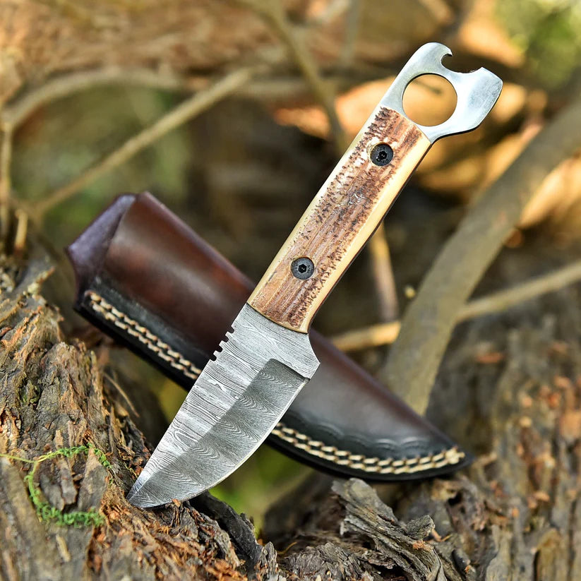 A fixed-blade knife with a patterned steel blade and a wood handle featuring a bottle opener attachment, resting on a log next to its brown leather sheath in an outdoor forest setting.