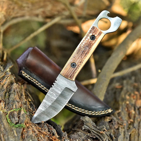 A fixed-blade knife with a patterned steel blade and a wood handle featuring a bottle opener attachment, resting on a log next to its brown leather sheath in an outdoor forest setting.
