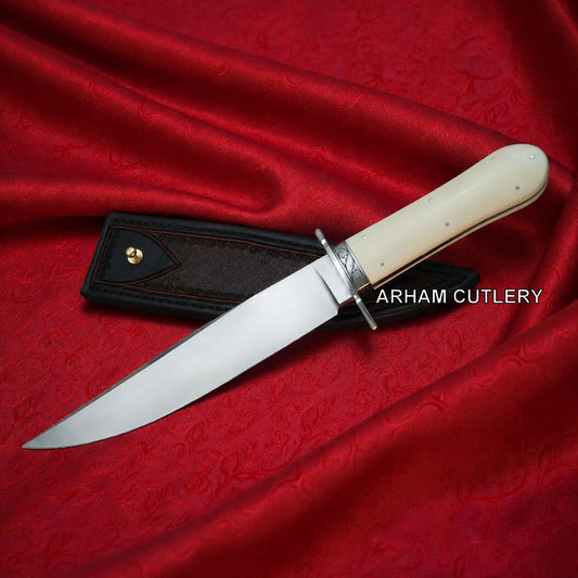 A fixed-blade knife with a polished silver blade, cream-colored bone handle, and silver guard, displayed diagonally on a textured red satin fabric next to its black leather sheath. The brand name 'ARHAM CUTLERY' is printed in white text over the handle area.
