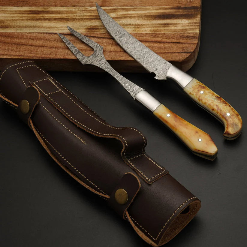 A set of three kitchen tools including a carving knife, a fork, and a butchory knife, displayed with their dark brown leather sheath on a dark surface next to a wooden cutting board. The knives feature patterned steel blades, silver bolster sections, and natural bone handles.