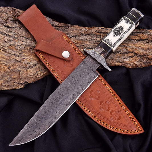A fixed-blade knife with a patterned steel blade, black and white handle, and a brown leather sheath, displayed on a piece of wood over black fabric.