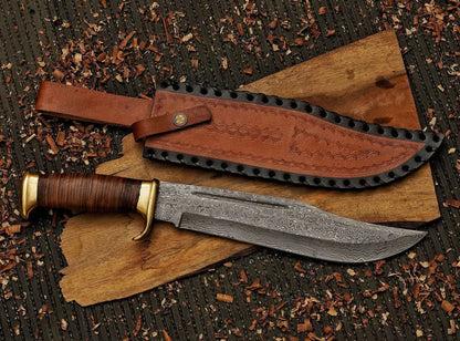 A fixed-blade knife with a patterned steel blade, brown wrapped handle, and brass guard, displayed next to its brown leather sheath on a piece of wood over a dark textured background.