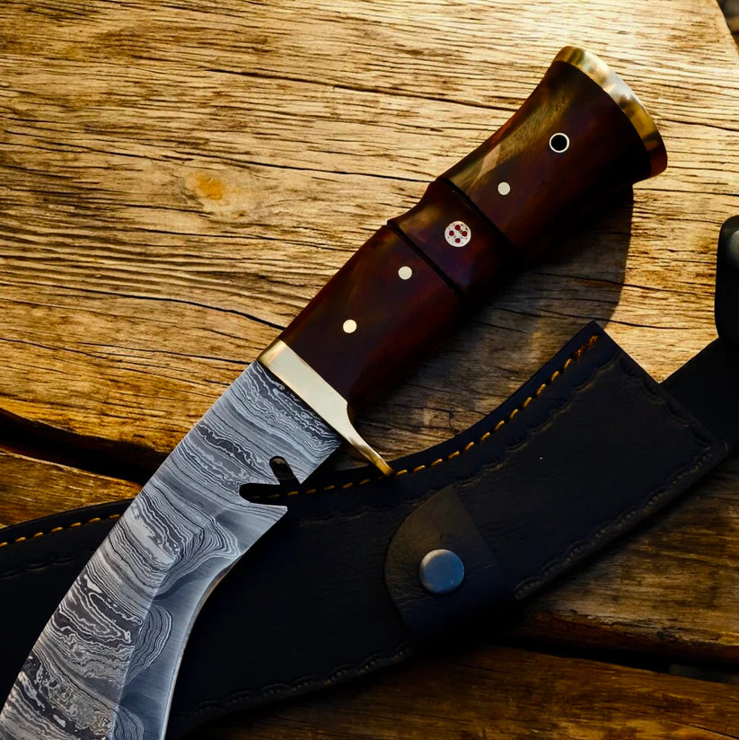 A fixed-blade knife with a patterned Damascus-style steel blade, a dark brown wooden handle with brass pins, and a black leather sheath, displayed on a rustic wooden surface.