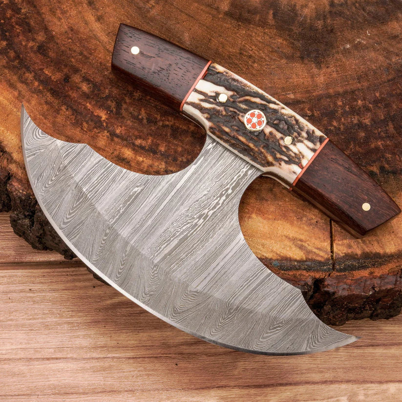 A handcrafted axe with a Damascus steel blade and a decorative handle made of dark wood and patterned bone, displayed on a rustic wood slice background.
