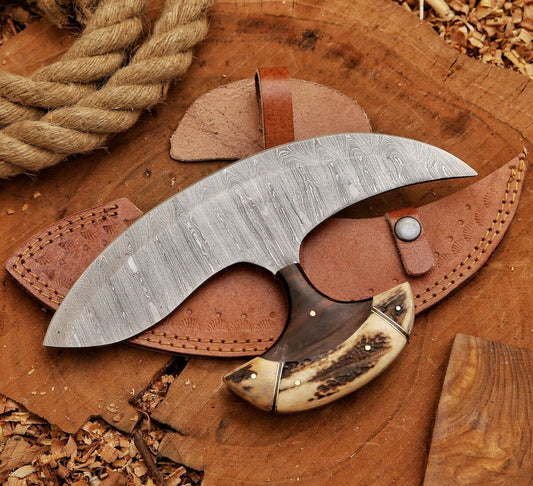 A curved Damascus steel hatchet with a textured patterned blade, a dark handle, and a bone-like pommel, displayed on a brown leather sheath over a rustic wood slice background.