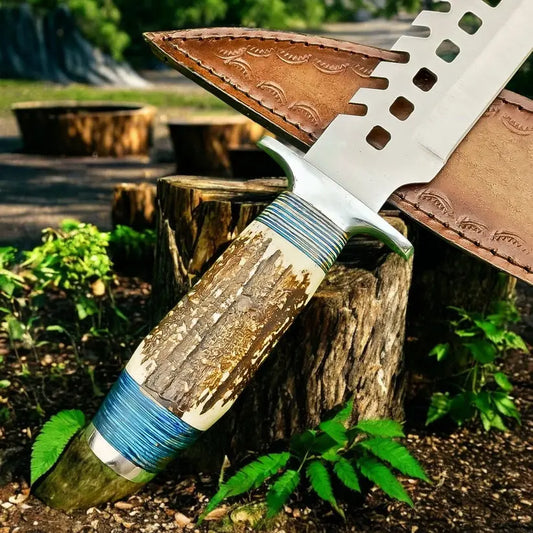 A large fixed-blade knife with a textured bone or antler-style handle wrapped in blue cord, shown resting on tree stumps outdoors with a brown leather sheath behind it.