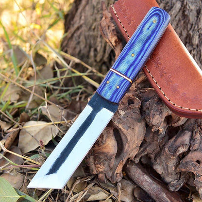 A fixed-blade knife with a blue marbled handle and a silver blade, resting on a brown leather sheath outdoors on a tree root.