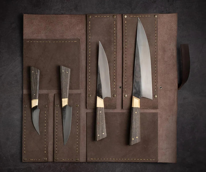 A set of four kitchen knives with dark wood handles and silver blades, displayed inside an open brown leather roll-up case on a dark textured background.