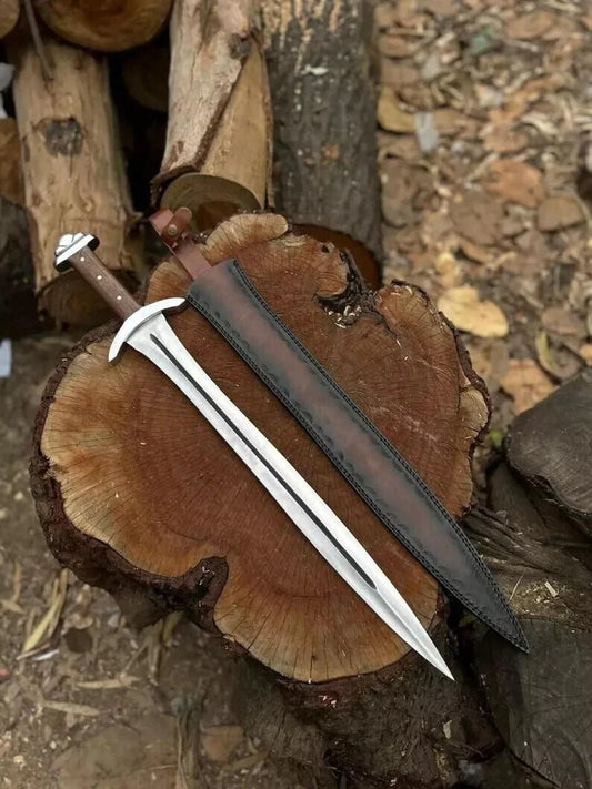 A short sword with a silver blade and brown handle, laid diagonally across a large cut tree stump next to its dark brown sheath, outdoors on a bed of logs and leaves.