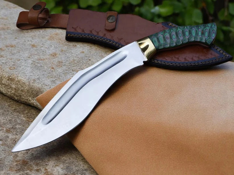 A fixed-blade knife with a polished silver blade, a gold-toned bolster, and a textured green handle, resting on a brown leather sheath over a tan leather surface.