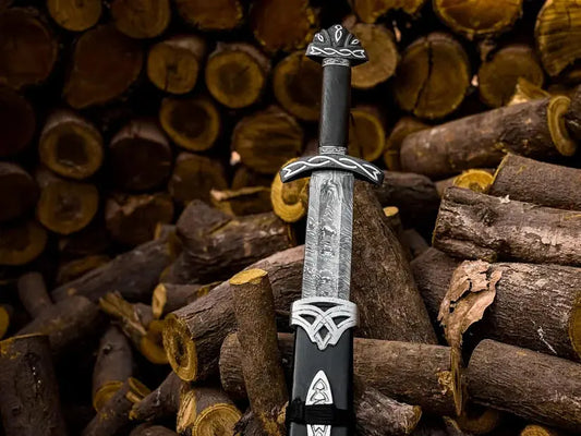 A decorative sword with a textured silver blade, black handle, and ornate silver guard and pommel, standing upright in a pile of cut logs.