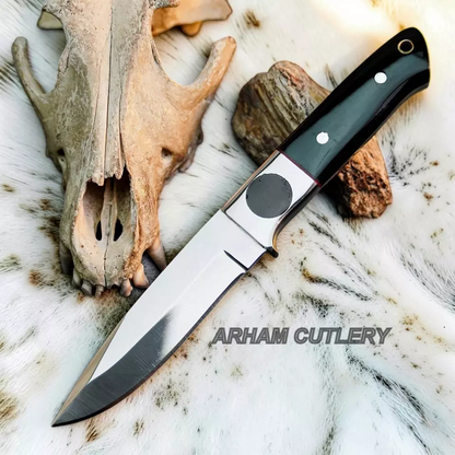 A fixed-blade knife with a polished silver blade and a black handle with silver rivets, laid diagonally on a white fur surface next to a deer skull and a rock. The text 'ARHAM CUTLERY' is overlaid on the image.