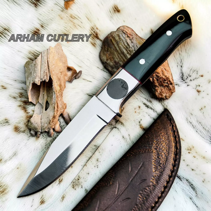 A fixed-blade knife with a polished steel blade, black handle scales, and silver rivets, displayed diagonally on a white fur background with animal bones, rocks, and a brown leather sheath. The text 'ARHAM CUTLERY' is visible in the upper left.