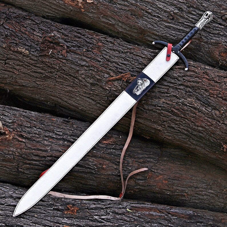 A long sword with a silver blade and black handle, resting diagonally on dark weathered logs with a small red loop and tan strap visible.