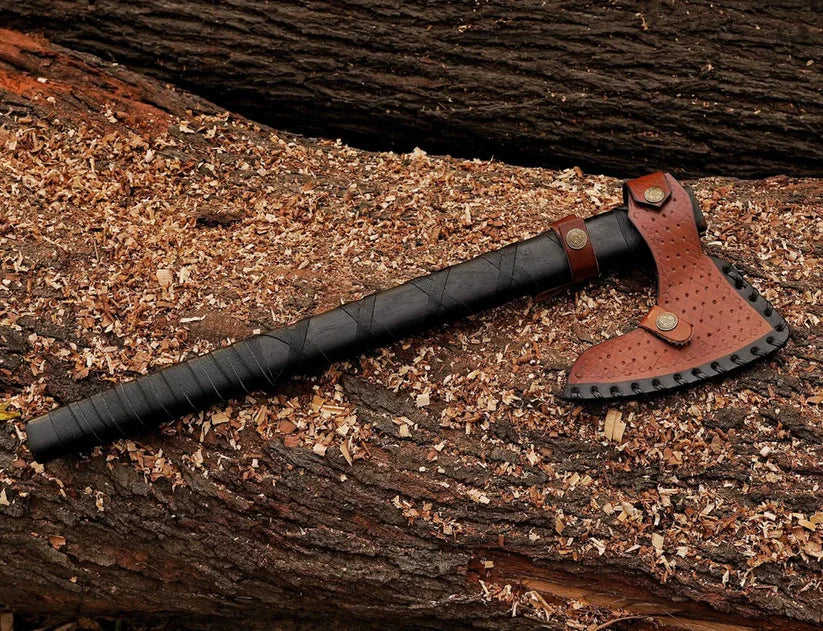 A black-handled axe with a brown leather blade cover resting on a log covered in wood shavings.