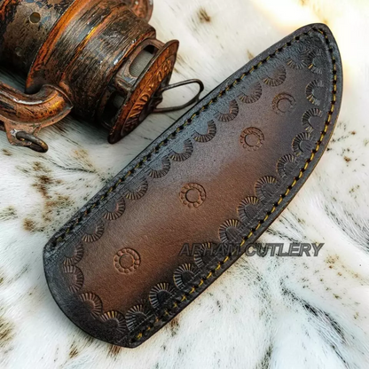 A dark brown leather knife sheath with hand-tooled circular patterns and yellow stitching, displayed on a white fur surface next to an antique wooden object. A watermark for 'ABAM CUTLERY' is visible.