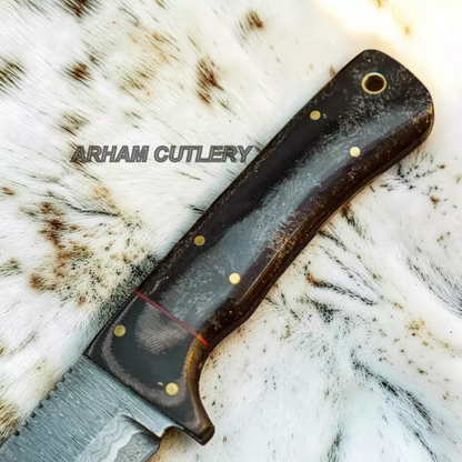 A close-up of a knife handle made of dark wood with brass pins, resting on a white and brown animal hide background. The brand name 'ARHAM CUTLERY' is watermarked across the center.