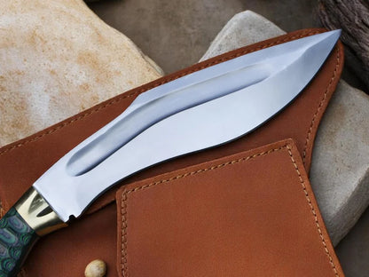 A close-up of a fixed-blade knife with a polished silver blade and a green patterned handle, resting on a brown leather sheath against a neutral stone background.