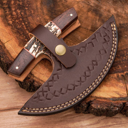A curved brown leather knife sheath with embossed geometric stitching and contrast stitching, shown with a partially unsheathed knife featuring dark wood handles and bone inlays, placed on a rustic wood log background.