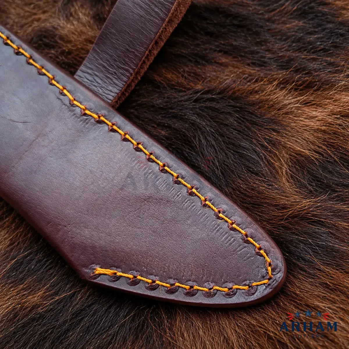 A close-up of a dark brown leather knife sheath with contrasting yellow stitching, laid on a textured brown fur surface. A small 'ABRAM' logo watermark is visible in the bottom right corner.